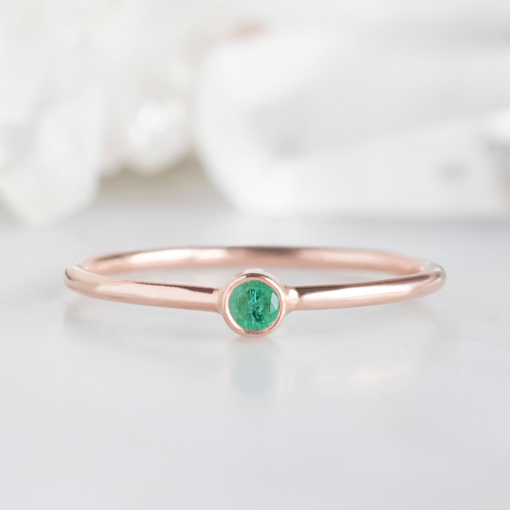 Custom Emerald Birthstone Stacking Ring | 10K Rose Gold. Displayed on marble surface with white burred background. 