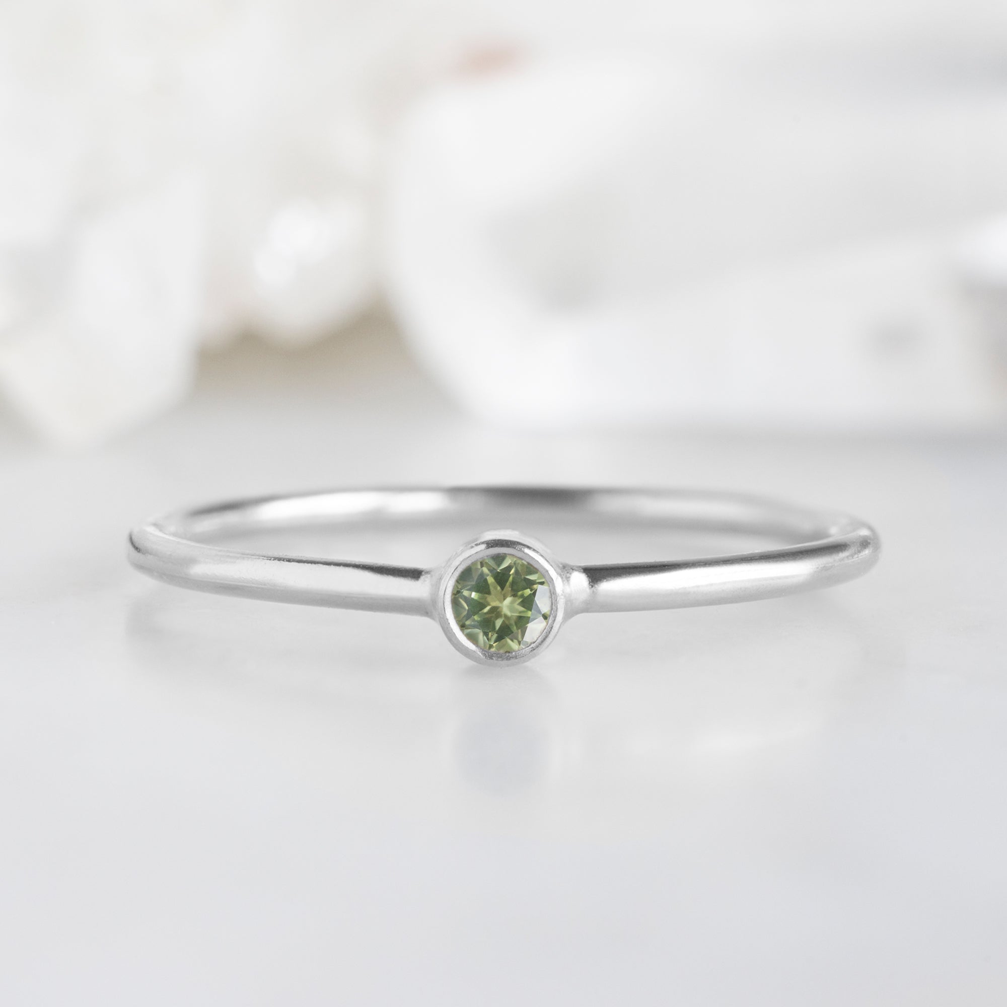 Custom Peridot Birthstone Stacking Ring | 10K White Gold. Displayed on marble surface with white blurred background. 