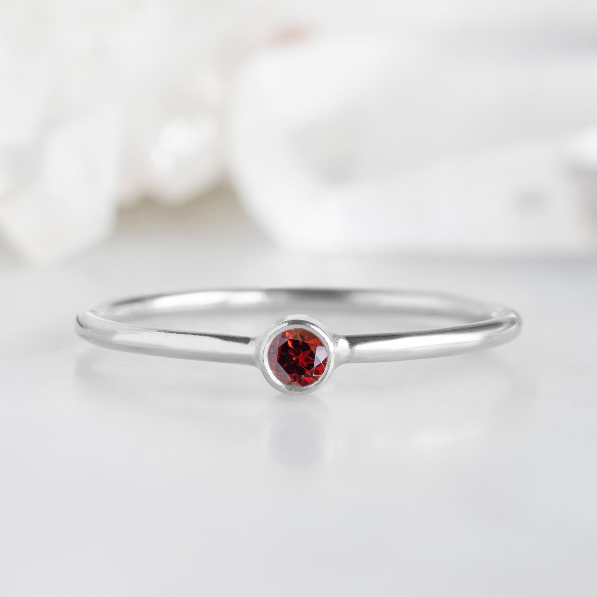 Custom Garnet Birthstone Stacking Ring | 10K White Gold. Displayed on marble surface with white blurred background. 