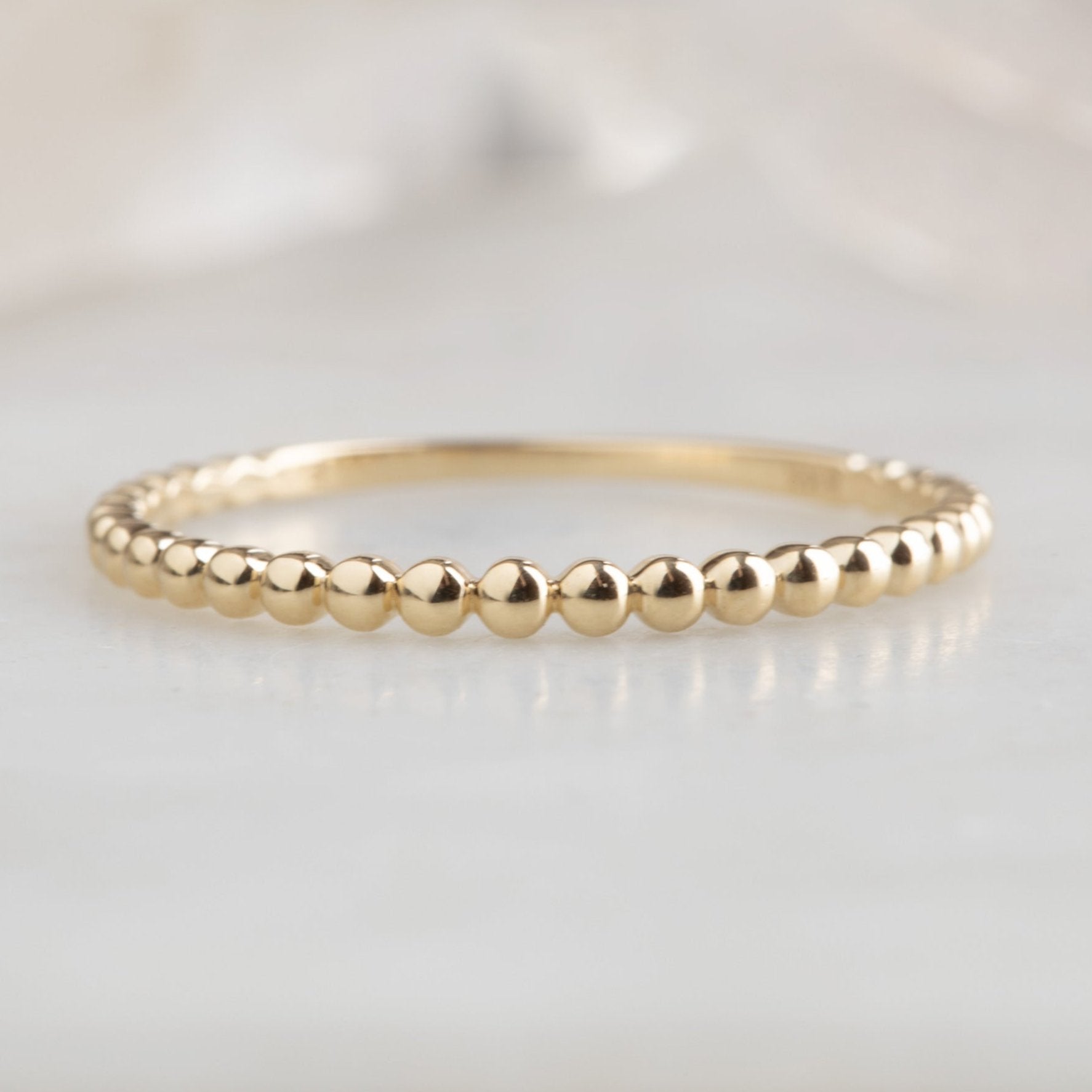 The Gold Beaded Stacking Ring in 14K Yellow Gold on White Marble