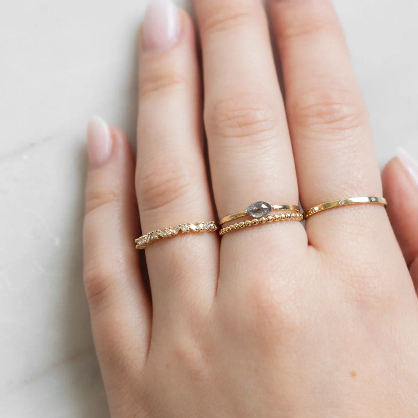 The Baguette Confetti Stacking Ring In Yellow Gold Displayed on Model's left hand ring finger alongside three other rings on consecutive fingers.