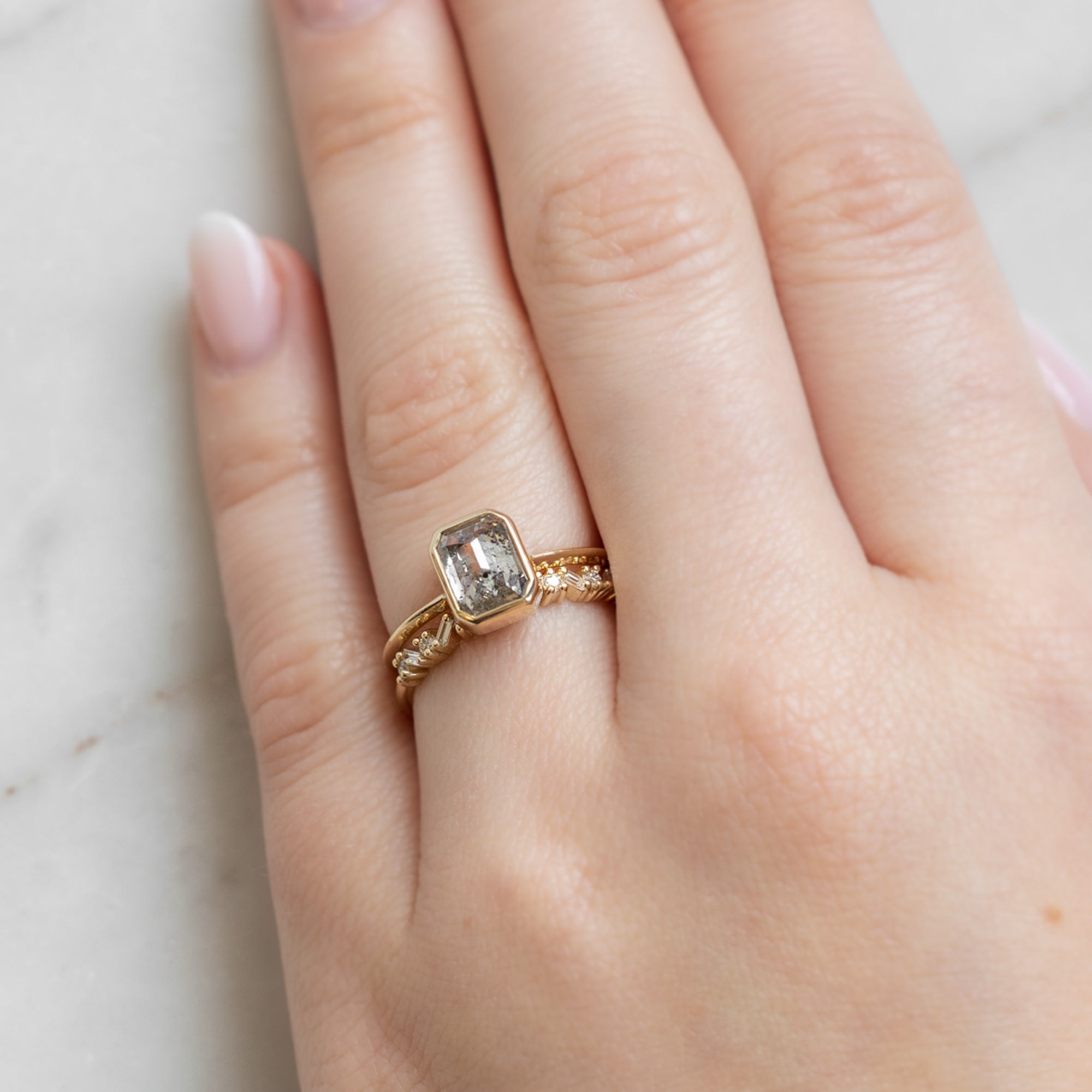 The Baguette Confetti Stacking Ring In Yellow Gold on Model's left hand ring finger paired with an Emerald Cut Bezel Set Diamond Engagement ring.