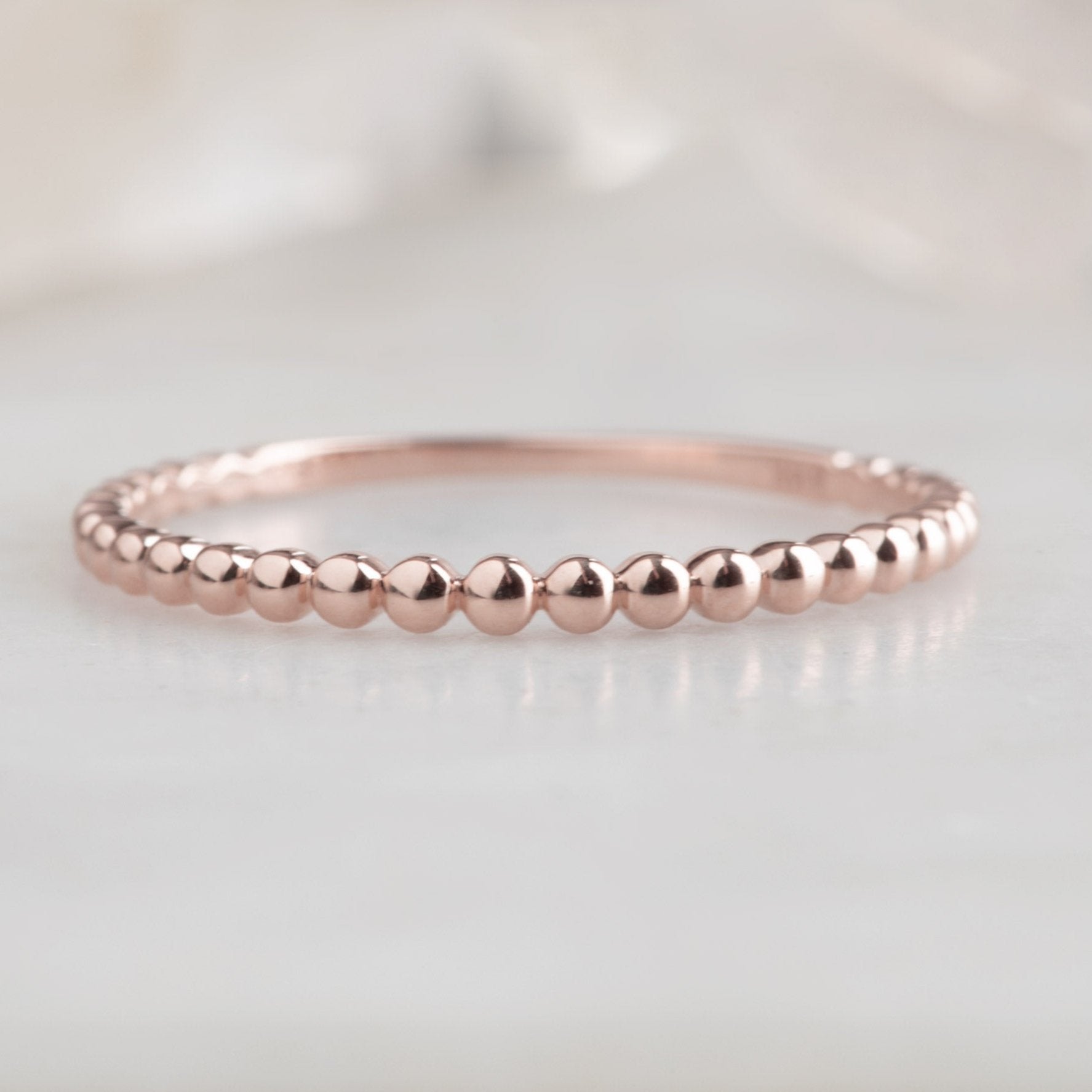 The Gold Beaded Stacking Ring in 14K Rose Gold on White Marble