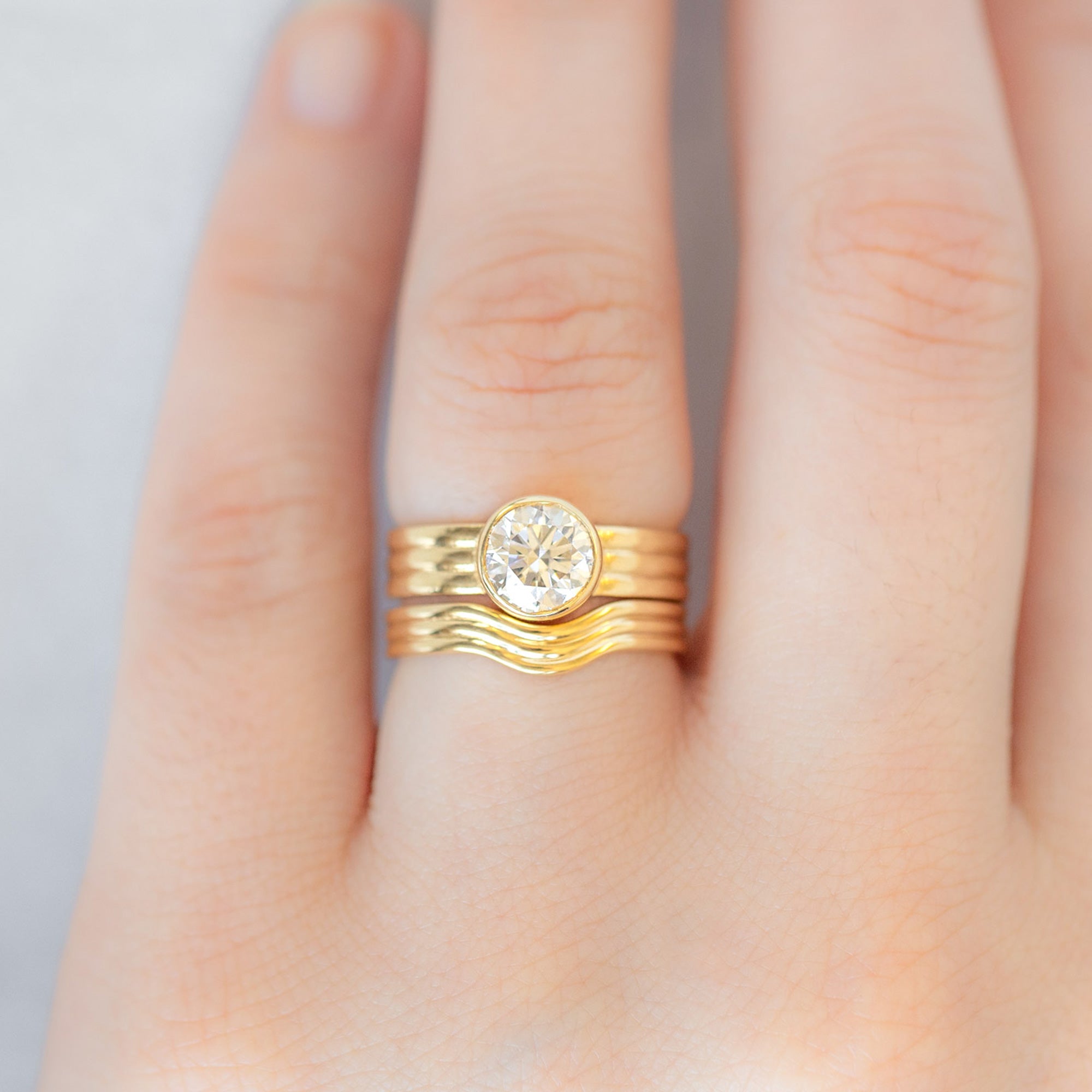 Custom Arc Stratum Stacking Band | 18K Yellow Gold displayed on model's left hand ring finger paired with matching engagement ring. 